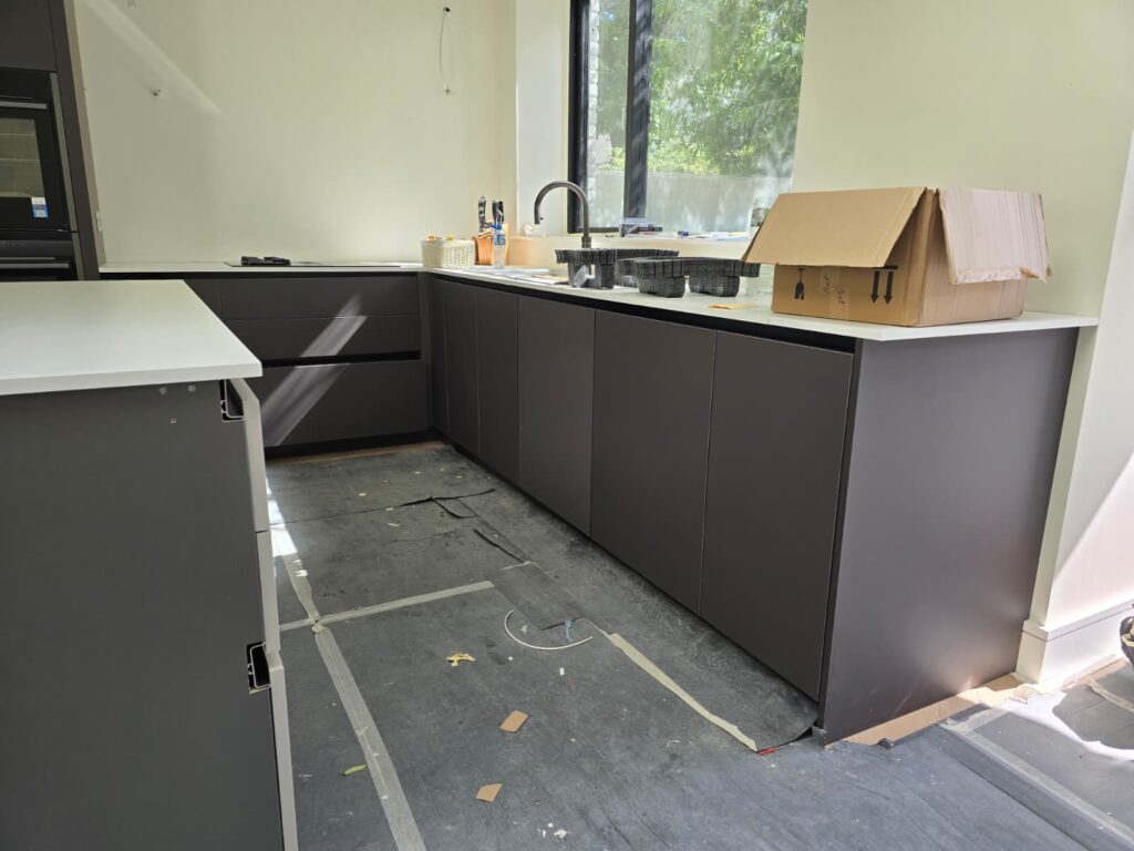 Bespoke dark kitchen cupboards beneath the window during installation