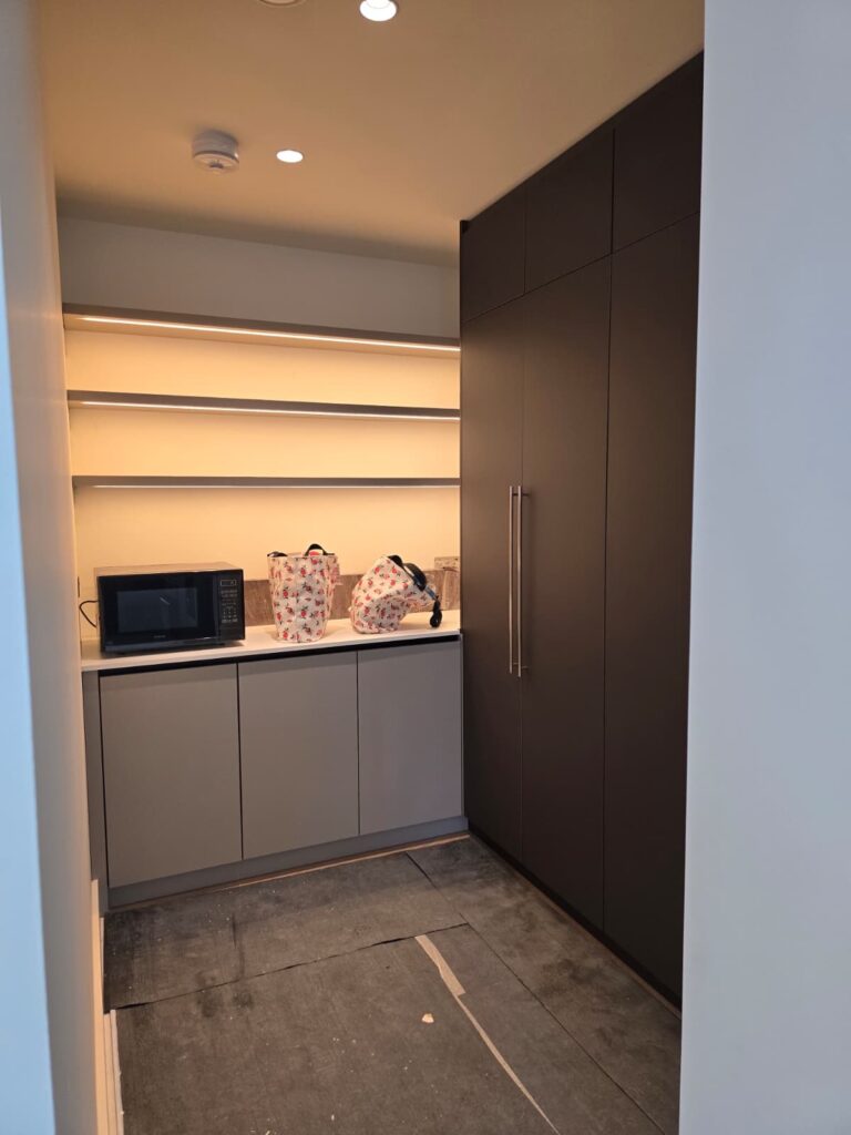 Fitted pantry with dark tall cupboards and illuminated open shelves